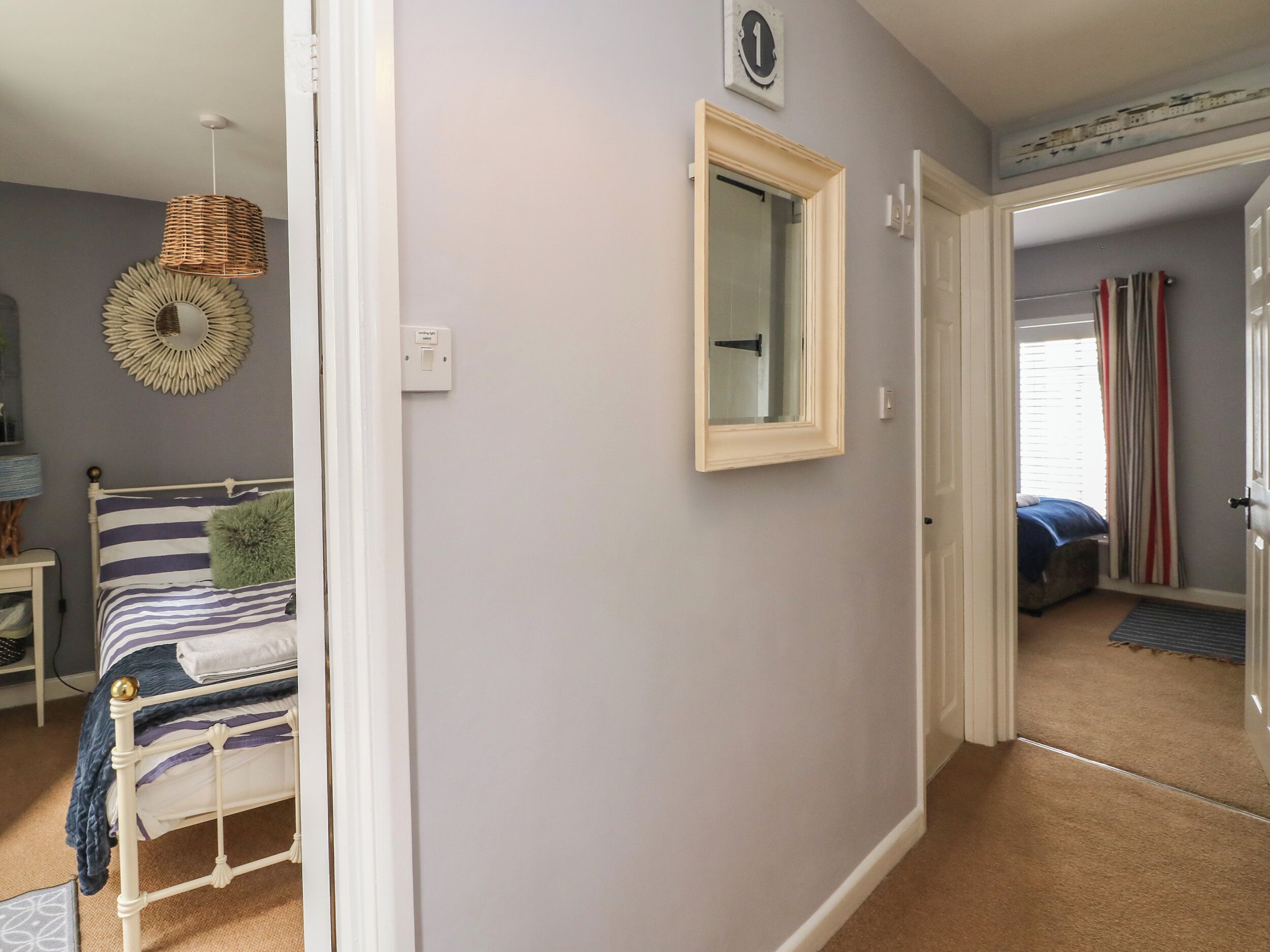 A bedroom with a bed, a bedside lamp, a mirror, and a door leading to another room.