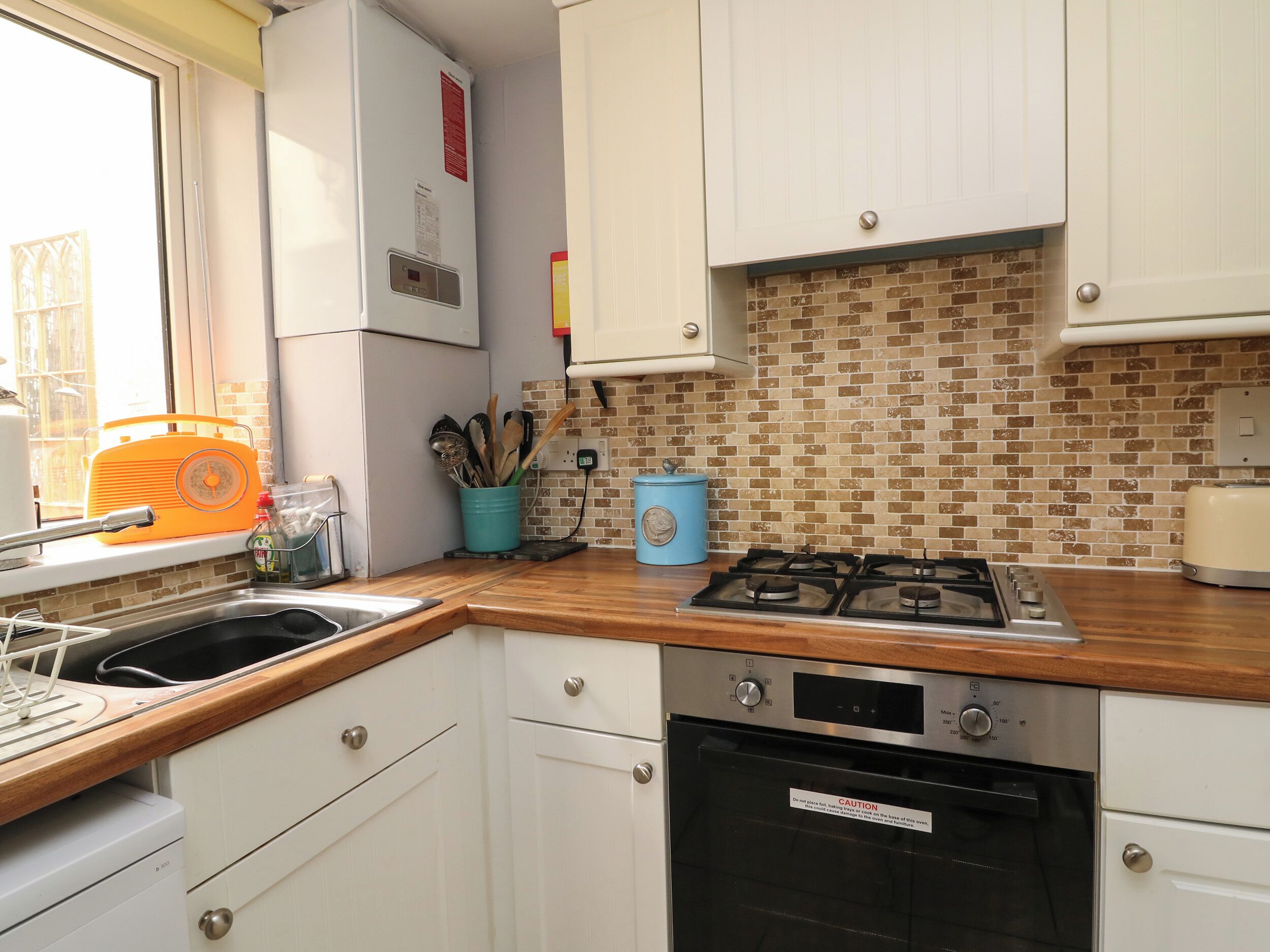 A kitchen with white cabinets, a brick backsplash, a gas stove, and a dishwasher.
