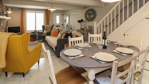 A dining area with a round table set for four, surrounded by white chairs. A sofa and a yellow armchair are visible in the background. - Harbour Reach (Weymouth)