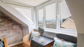 A room with a sloped ceiling, a brick wall, a black table with a mirror, and a view of the sea through large windows. - Harbour Reach (Weymouth)