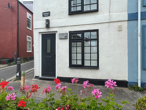 A white building with a black door and windows, a sign reading "Harbour Reach", and red flowers in the foreground. - Harbour Reach (Weymouth)