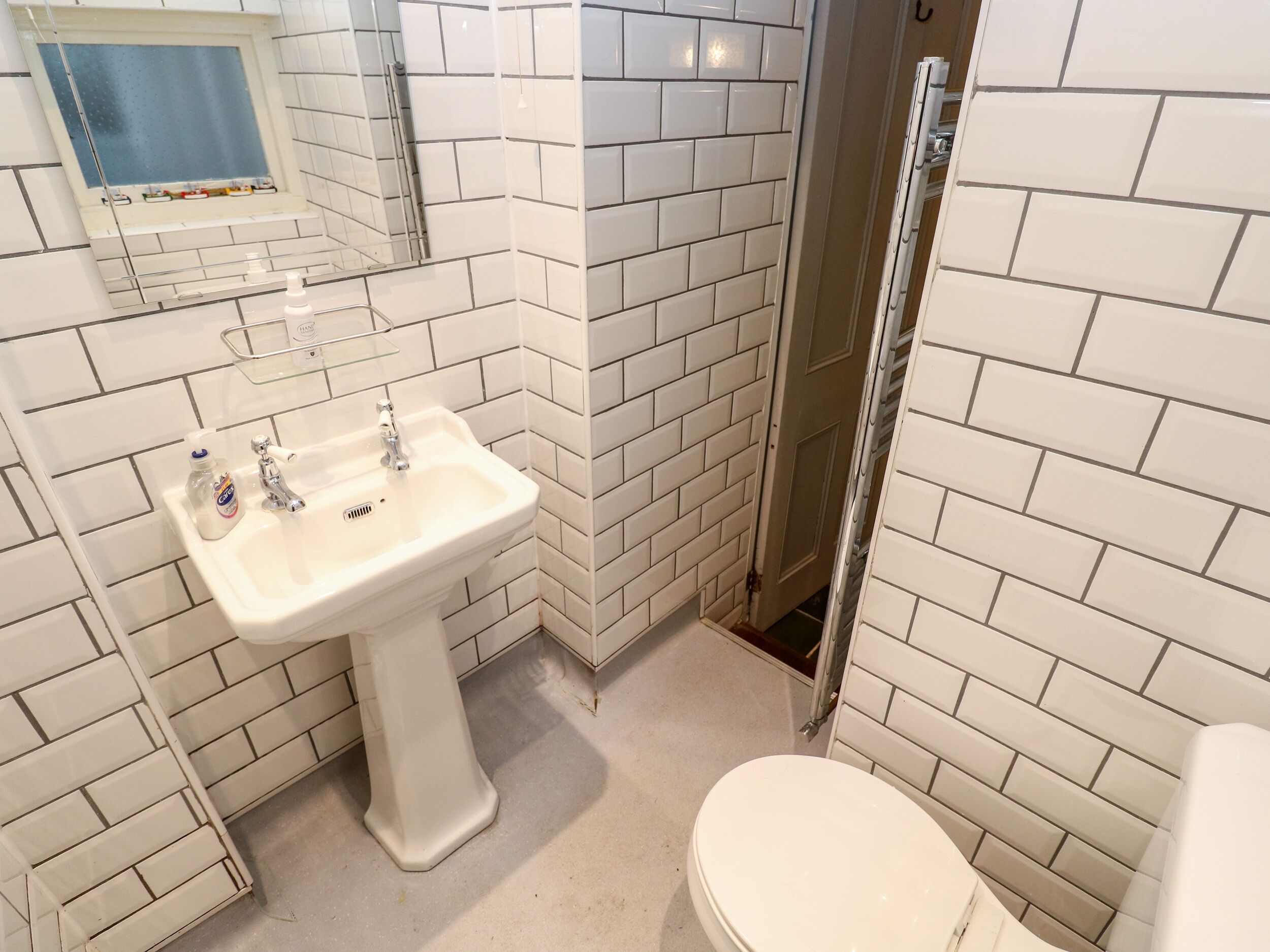 A bathroom with white subway tiles, a white sink, a mirror, and a toilet.