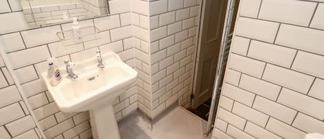 A bathroom with white subway tiles, a white sink, a mirror, and a toilet.