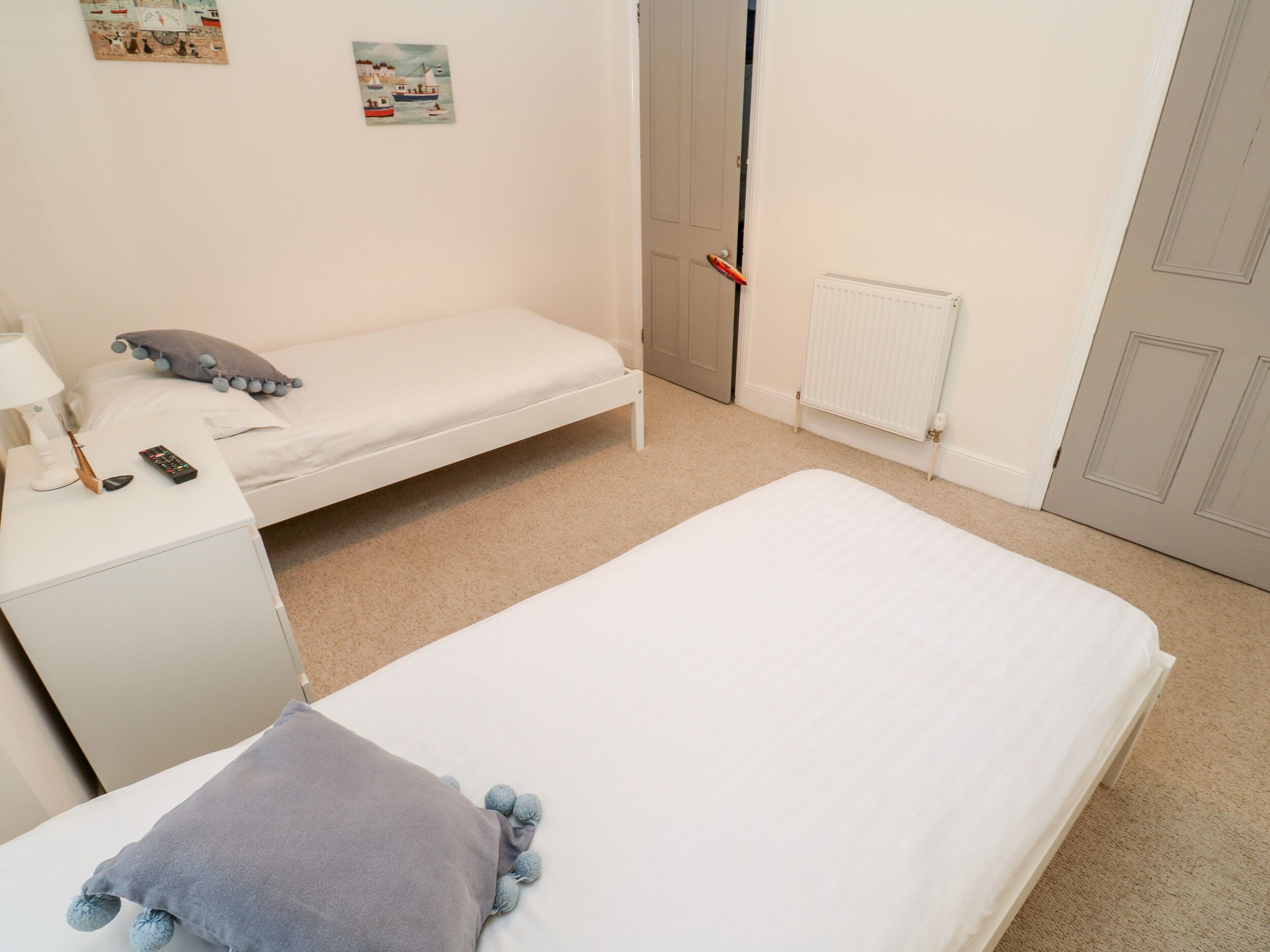 A small, neatly arranged bedroom with a single bed, a bedside table with a lamp, and a small desk with a remote control.