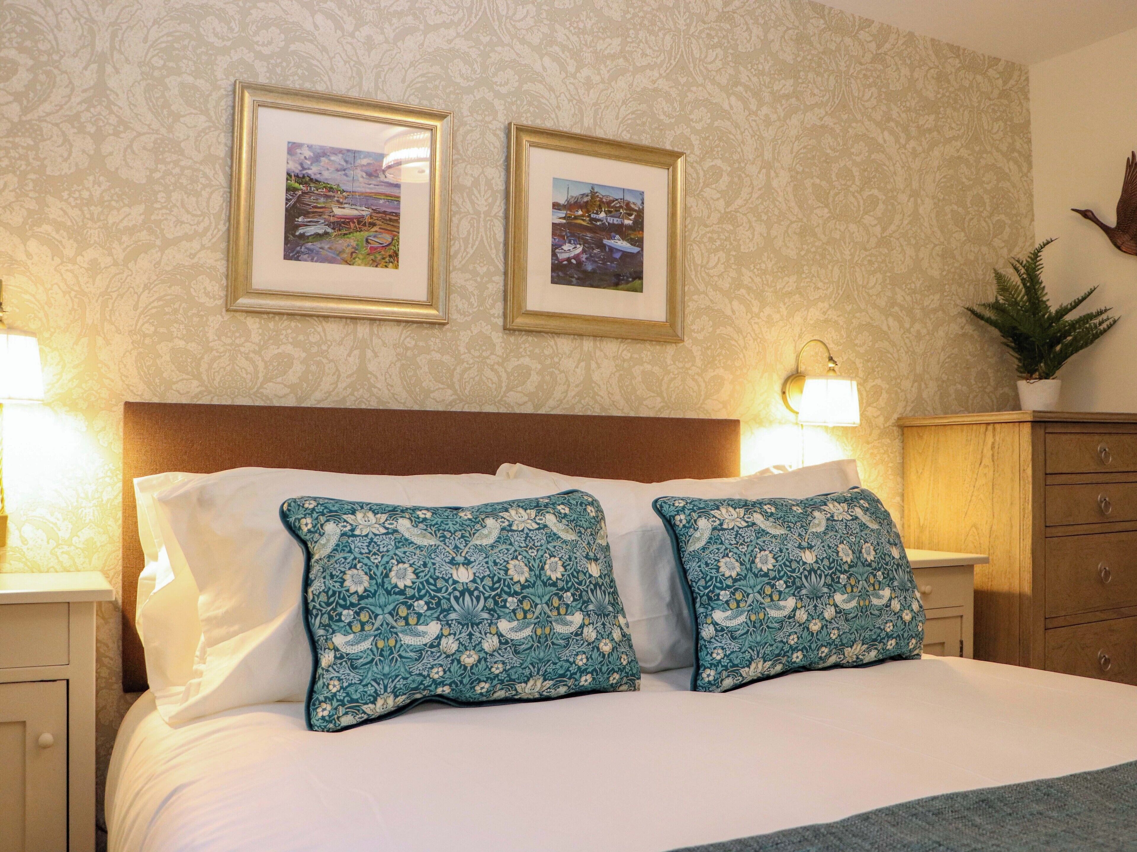 A neatly made bed with white and blue patterned pillows, a wooden headboard, and two framed pictures on the wall.