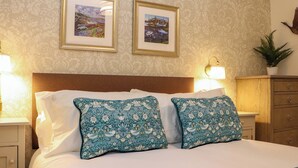 A neatly made bed with white and blue patterned pillows, a wooden headboard, and two framed pictures on the wall. - Paye House - Cromarty (Cromarty)