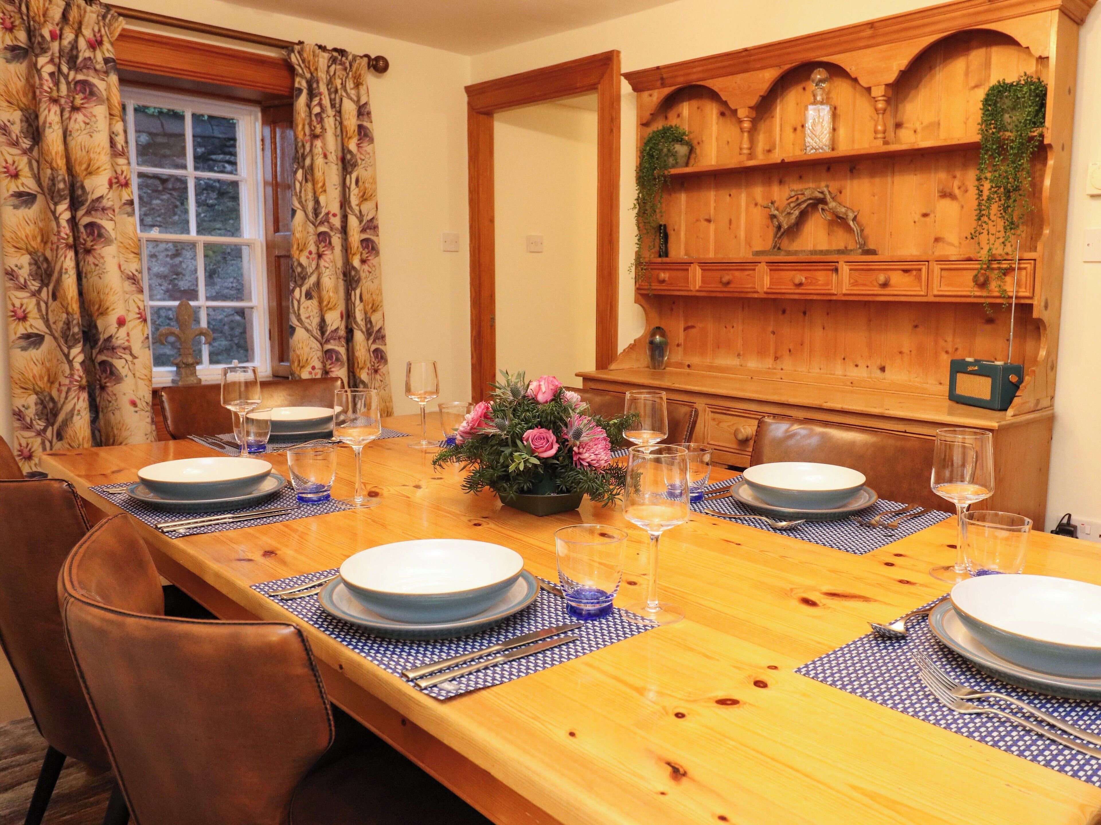 A dining room with a long wooden table set for four, surrounded by chairs.