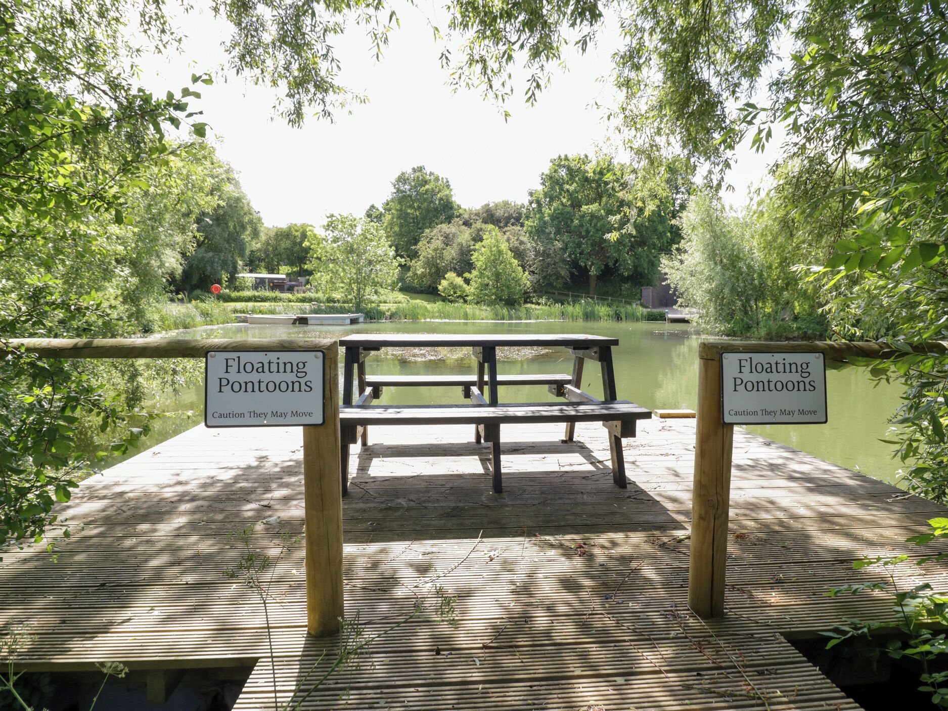 Un muelle de madera con una mesa de picnic y dos letreros que advierten sobre pontones flotantes.