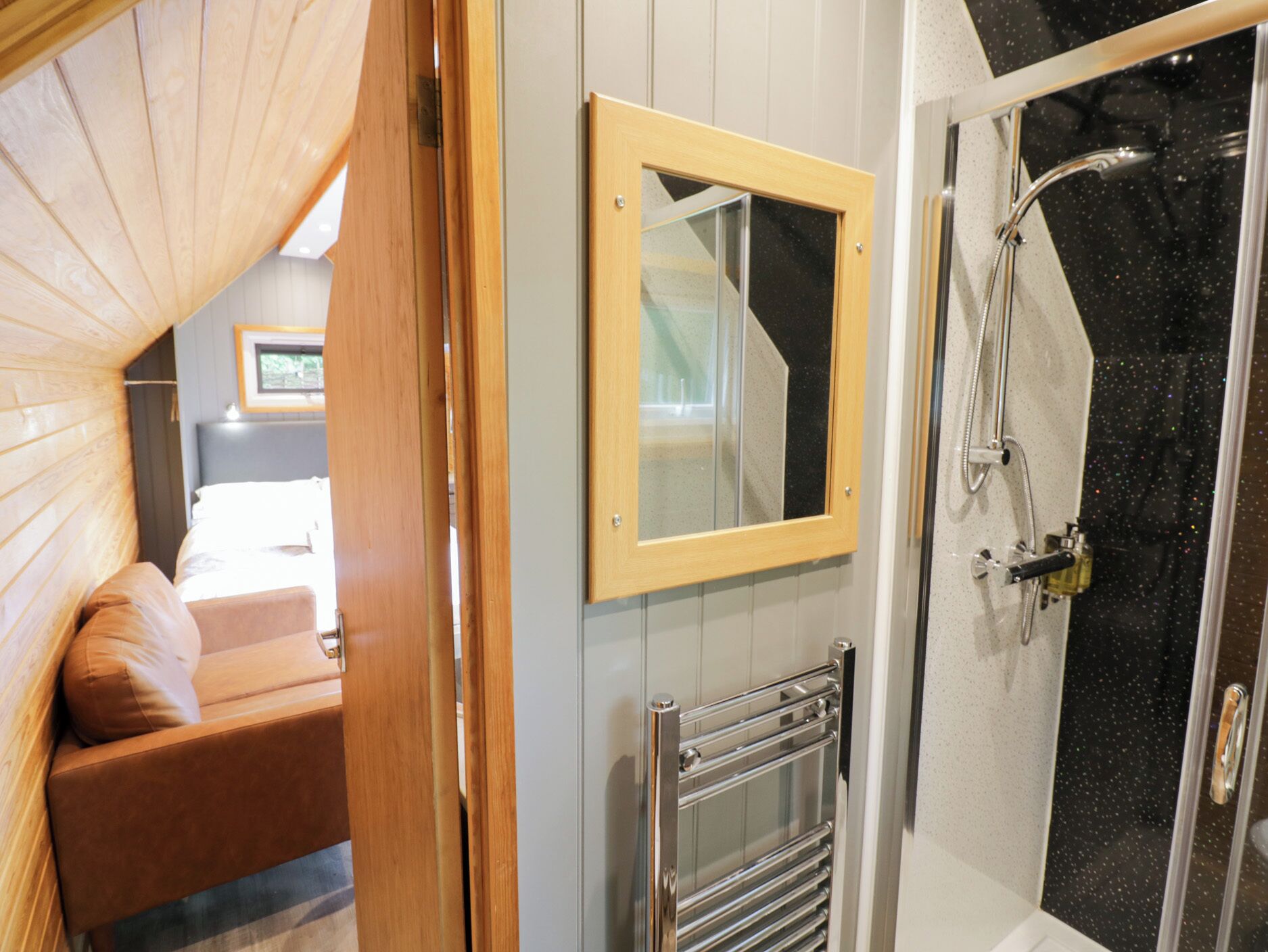 Une salle de bain avec une douche, un porte-serviettes et un miroir encadré en bois.