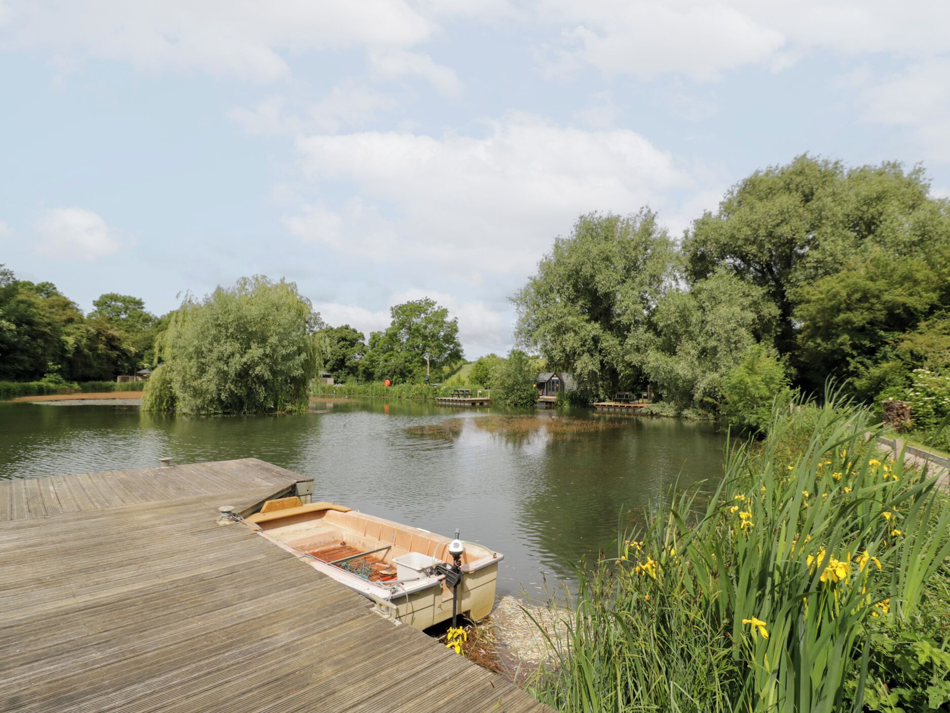 A wooden dock extending into a calm lake, surrounded by lush greenery and trees.
