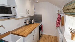 Cocina compacta con armarios blancos, encimera de madera, microondas, hervidor y tostadora.