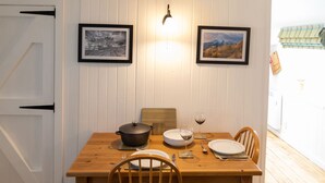 Un comedor con una mesa de madera, dos sillas, una olla, una copa de vino y un bol. Hay dos cuadros en la pared.