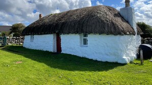 Una casa tradicional con techo de paja, fachada blanca, puerta roja y chimenea.
