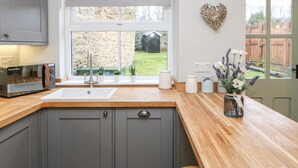 Una cocina moderna con armarios grises, encimera de madera, un tostador empotrado, un fregadero y una ventana con vistas a un jardín.
