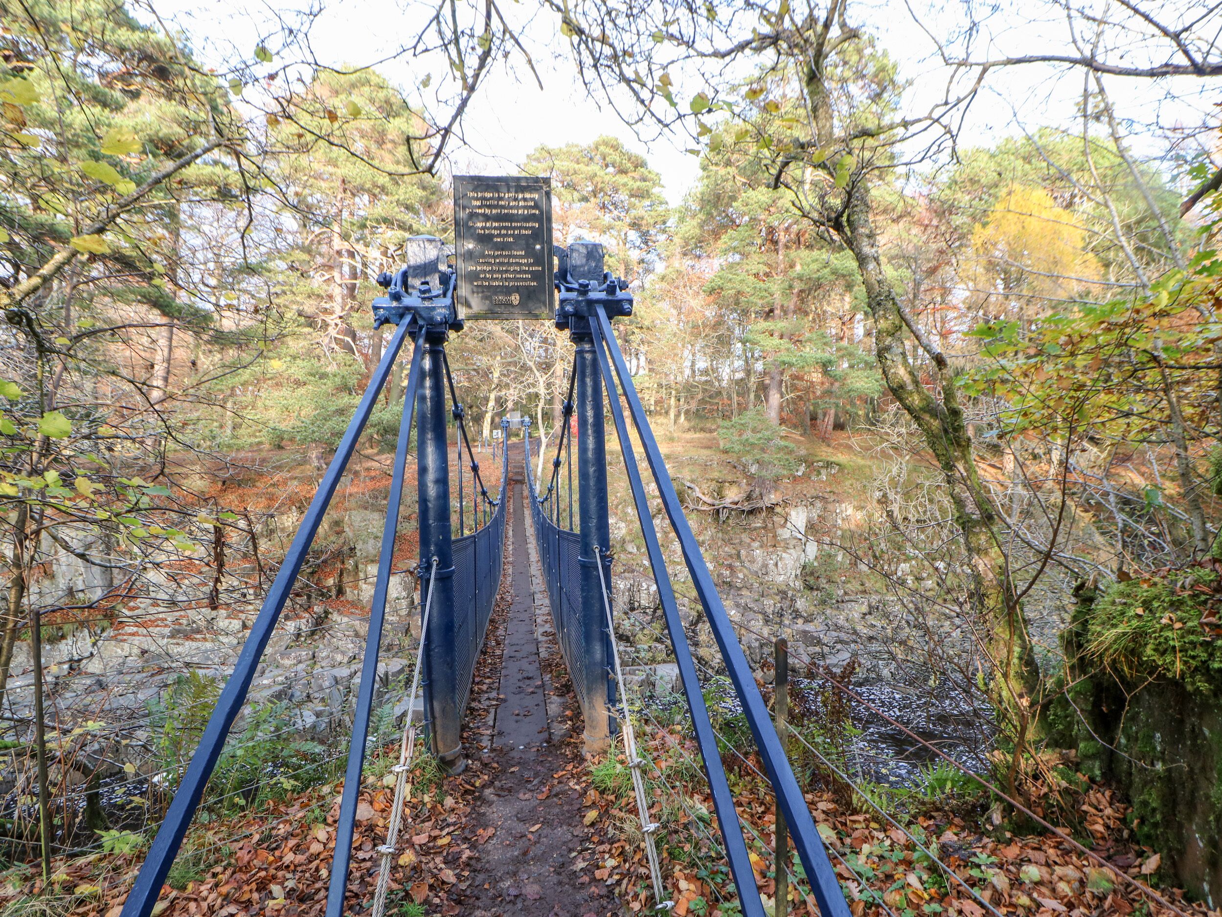 A suspension bridge with a signpost in a forested area.