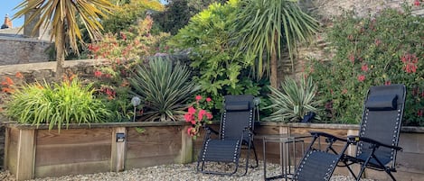 Un jardín con diversas plantas y un espacio de descanso con sillas y una mesa.