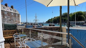 A terrace with metal tables and chairs, overlooking a marina with boats and a tall ship. - Seasides (Weymouth)