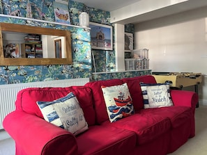 Un sofá rojo con almohadones decorativos, un espejo de madera y una pared con papel tapiz de temática náutica.