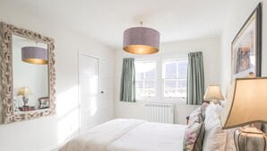 A hotel room with a large bed, a mirror, a window with curtains, a radiator, and a lamp. - Stalker's Cottage - Torridon (Achnasheen)