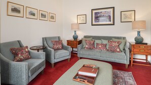 A living room with two grey armchairs, a grey sofa, and a red carpet. There are framed pictures on the walls and two lamps on side tables. - Stalker's Cottage - Torridon (Achnasheen)