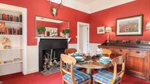 A dining room with a red wall, a fireplace, a chandelier, and a dining table set for four. - Stalker's Cottage - Torridon (Achnasheen)
