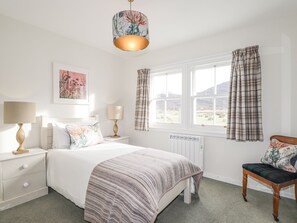 A bedroom with a bed, two bedside tables with lamps, a chair, a window with curtains, and a radiator. - Stalker's Cottage - Torridon (Achnasheen)