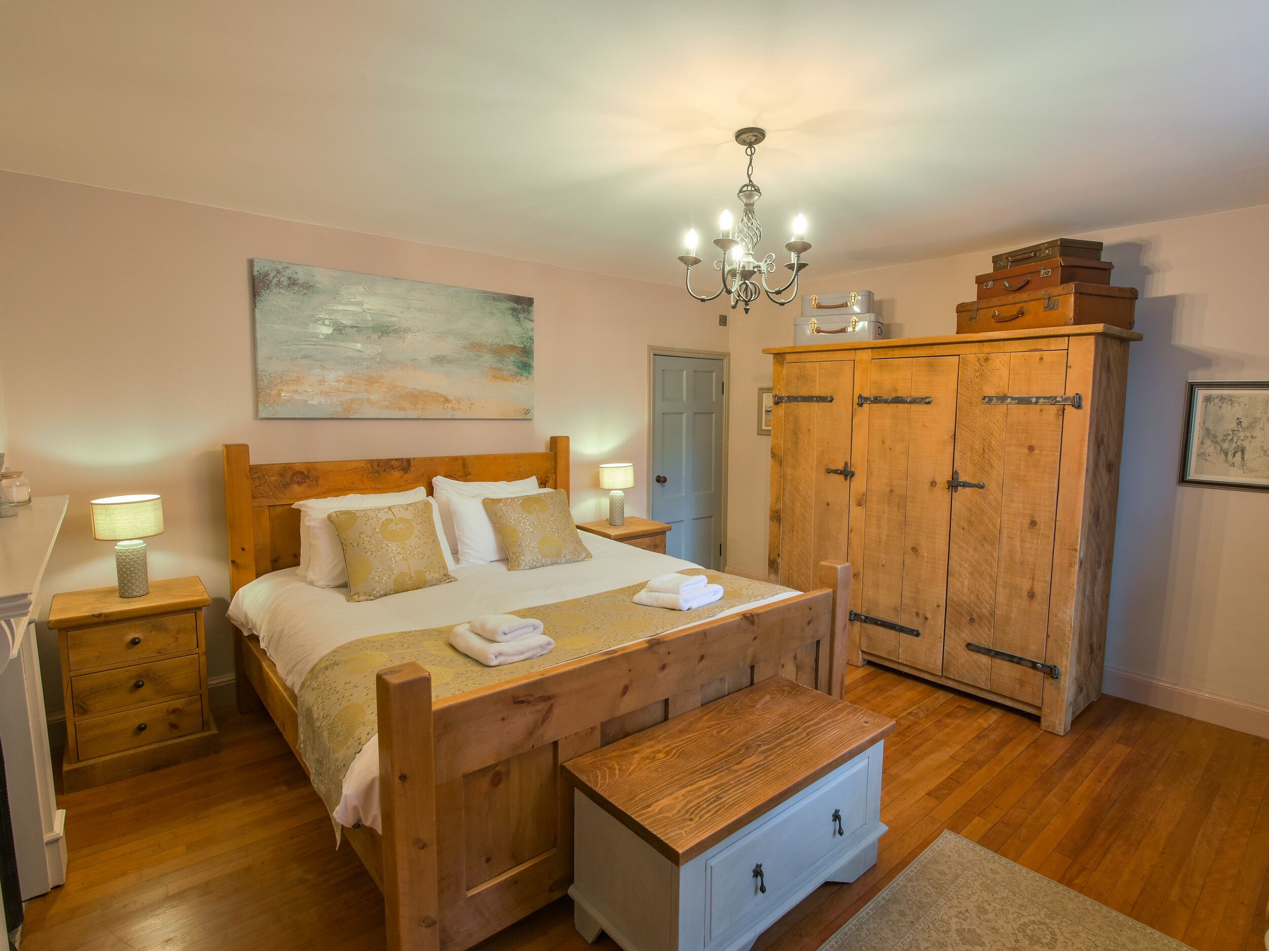 Un dormitorio con una cama de madera, lámparas de noche, un candelabro, un armario y un cuadro en la pared.