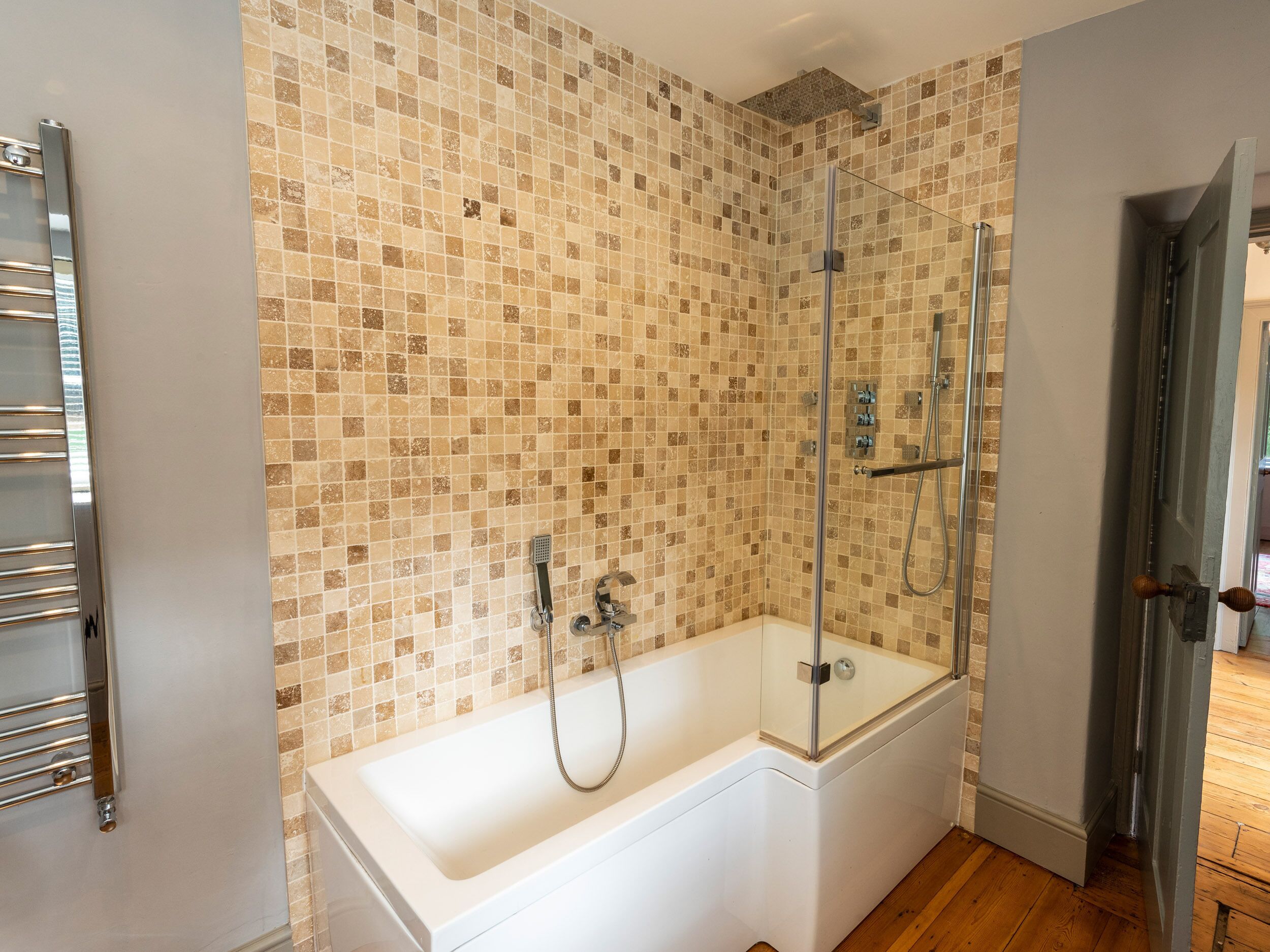 A bathroom with a glass-enclosed shower, a white bathtub, and a tiled wall.