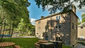 Un edificio in pietra con un cortile erboso, tavoli da picnic e barbecue.