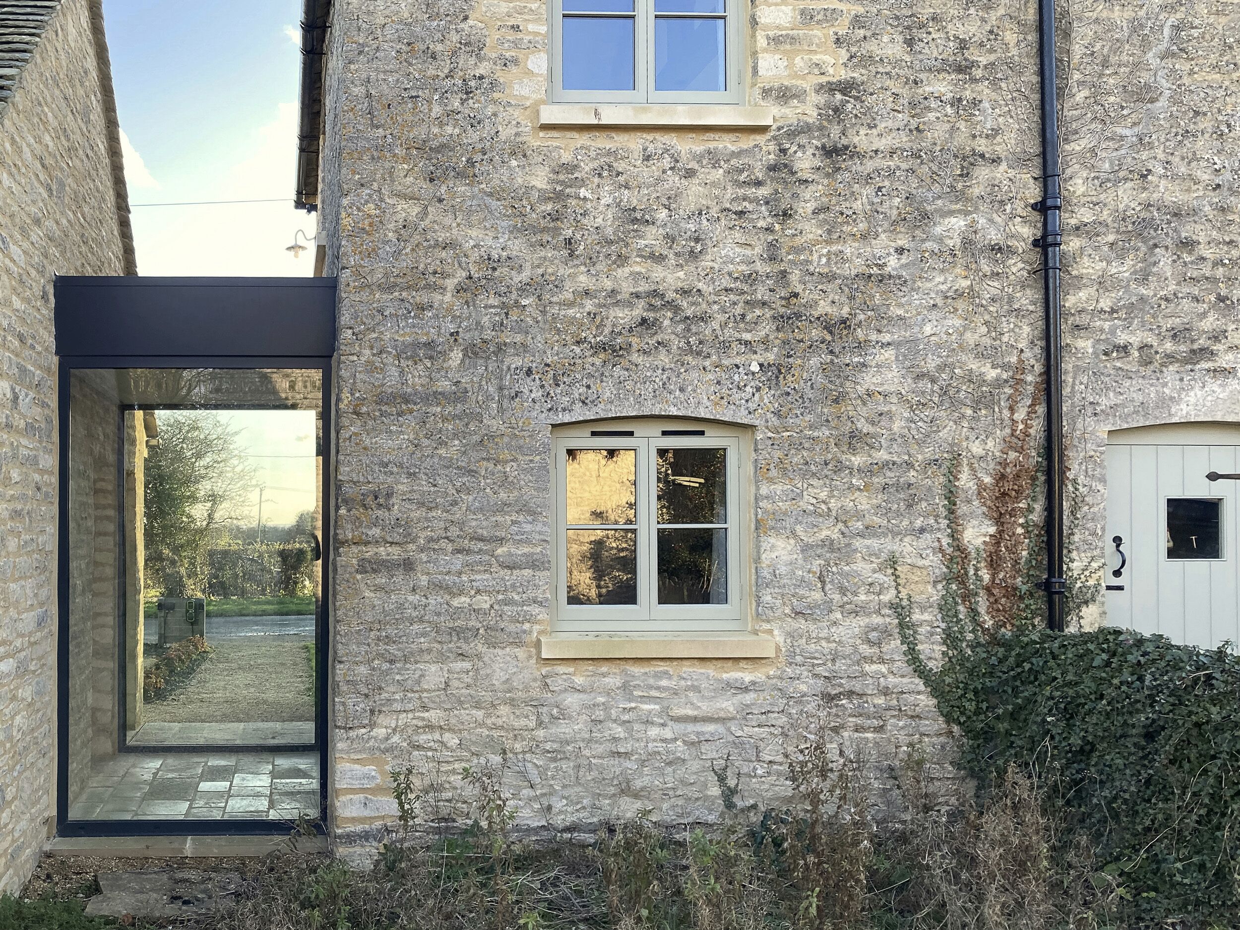 A stone building with a modern glass entrance, a small window, and a door.