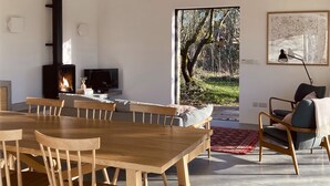 A modern dining area with a wooden table and chairs, a fireplace, and a view of the outdoors. - High Cogges Farm Holiday Cottages The Cart Shed (Witney)