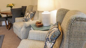 A living room with a sofa set, a table with chairs, a lamp, and a vase with flowers. - Beechgrove Cottage - Pitmedden Gardens (Ellon)