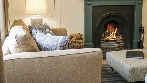 A cozy living room with a fireplace, a sofa, an ottoman, and a lamp. - Beechgrove Cottage - Pitmedden Gardens (Ellon)