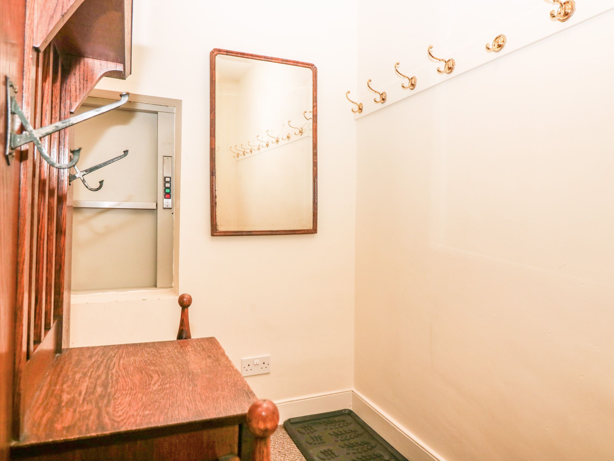 A wooden table with a metal hook, a wall-mounted mirror, and a coat rack with hooks.