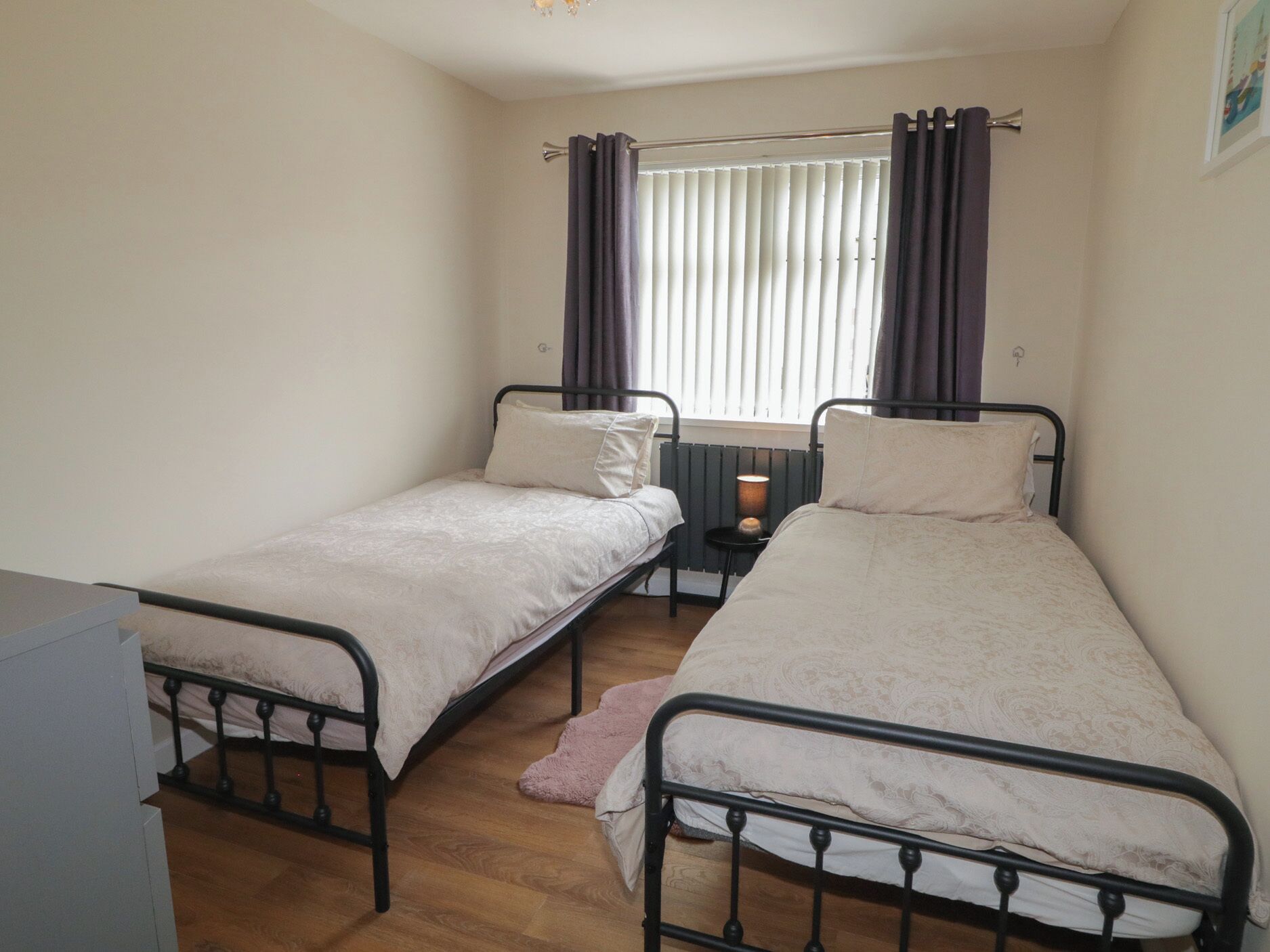 A small, single-room accommodation with two single beds, a small table, and a window with curtains.