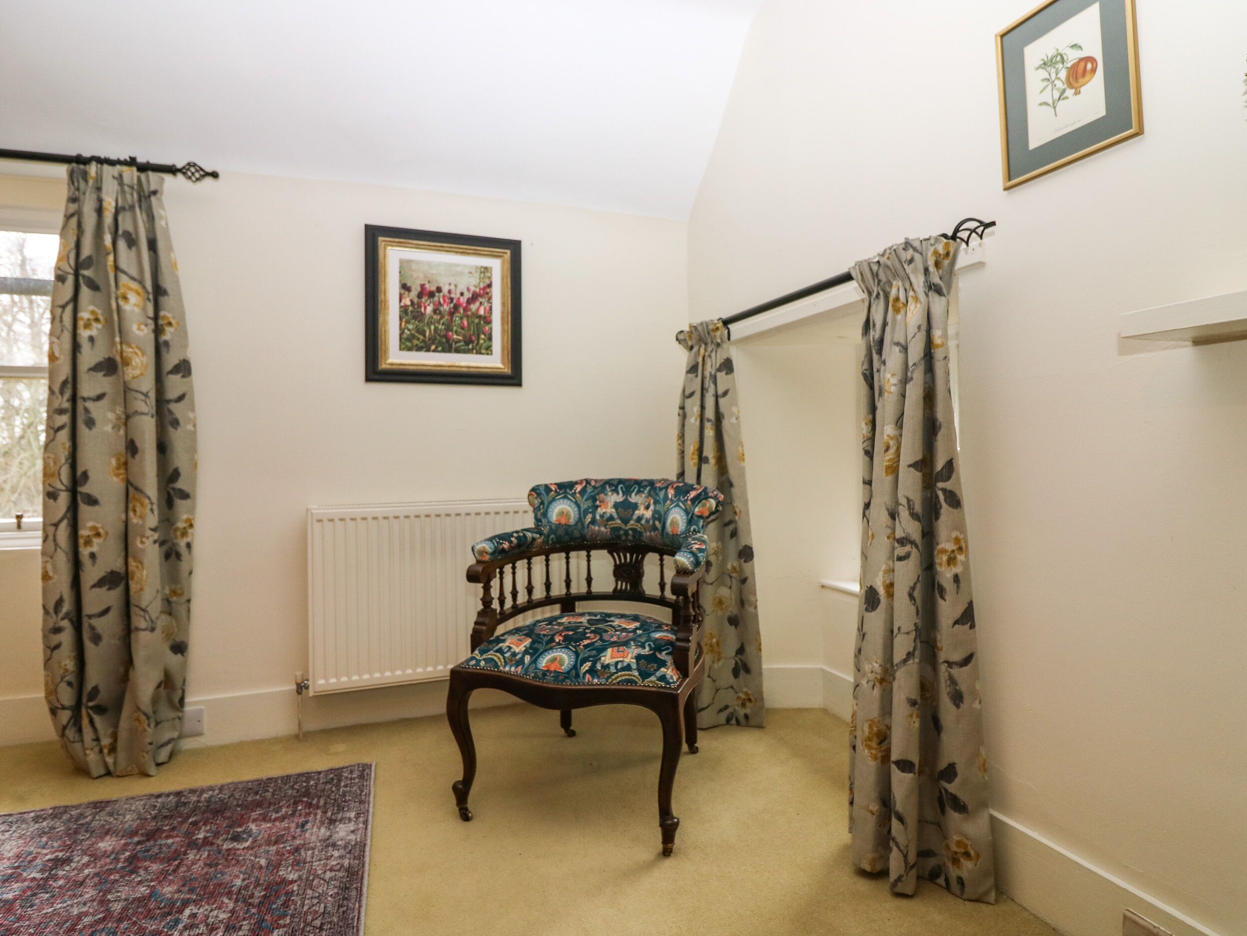 A room with a floral-patterned chair, a radiator, and a framed botanical illustration on the wall.