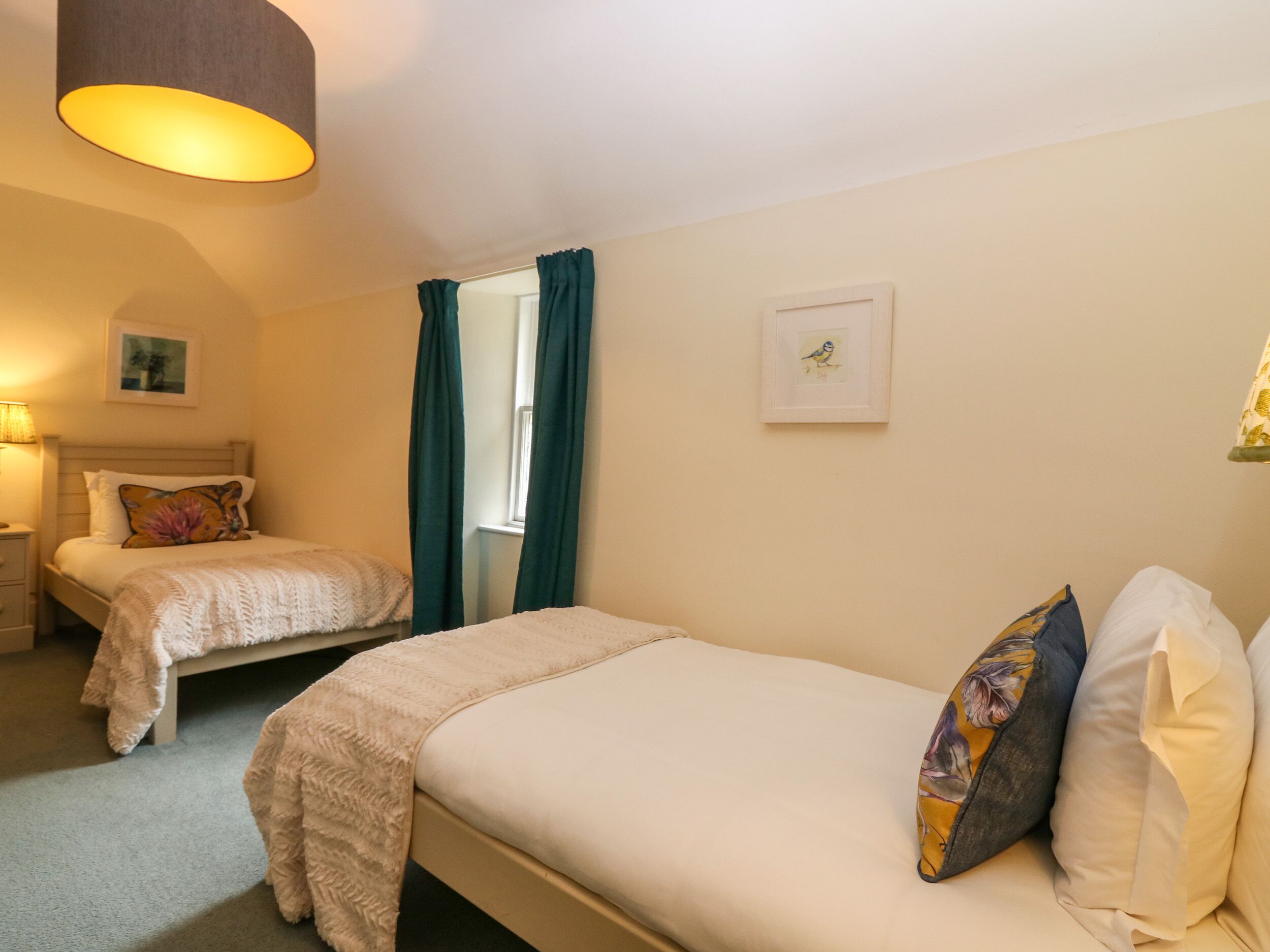 Ein Hotelzimmer mit zwei Einzelbetten, einem Nachttisch mit Lampe, einem gerahmten Bild an der Wand und einem Fenster mit Vorhängen.