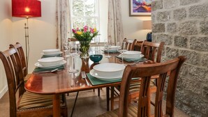 A dining room with a wooden table set for six, surrounded by chairs. There is a vase with flowers on the table, and a lamp to the left. - Steading Cottage - Craigievar Castle (Alford)