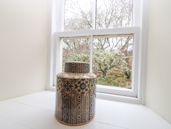 Un vase en céramique orné de motifs complexes, posé sur un rebord de fenêtre peint en blanc.