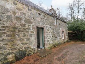 A stone building with a single door and a small window, surrounded by a dirt path and trees. - North Mains Cottage - Craigievar Castle (Alford)