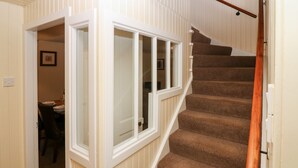 A staircase with carpeted steps and a wooden handrail, leading to a room with a dining area visible through an open door.