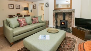 A living room with a sofa, ottoman, fireplace, television, and a clock on the wall.