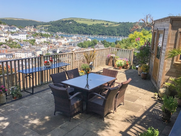 Un balcon agrémenté de meubles en osier, de plantes en pot et offrant une vue sur la ville et les collines.