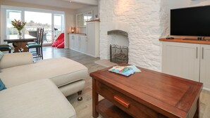 Een moderne woonkamer met een stenen haard, een televisie en een eethoek met een rode stoel.