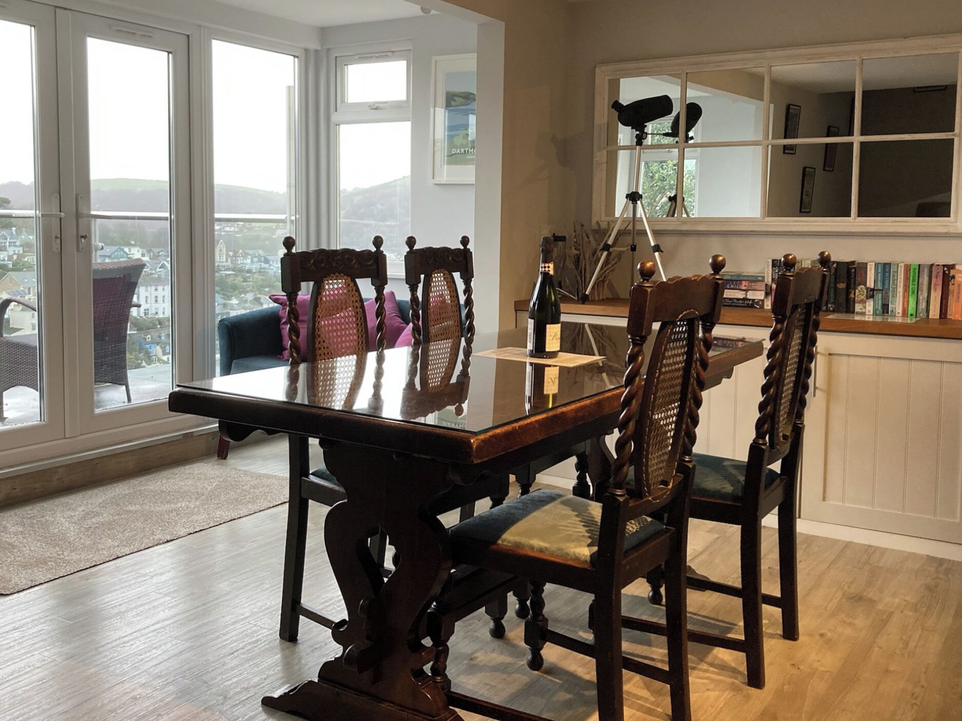 A dining area with a glass-top table, wooden chairs, and a telescope on a tripod.