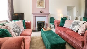 Un salon avec deux canapés rouges, un pouf vert, une cheminée rose et un tableau accroché au mur.