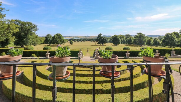 Un jardin aménagé avec plusieurs plates-bandes fleuries en terrasses et une vue lointaine sur des collines ondoyantes.