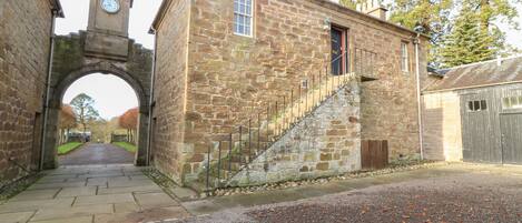 A stone building with a clock tower, a staircase, and a paved road leading through an archway.