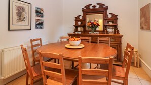 Une salle à manger avec une table en bois entourée de chaises, un miroir au-dessus de la table et des œuvres d’art encadrées accrochées aux murs.