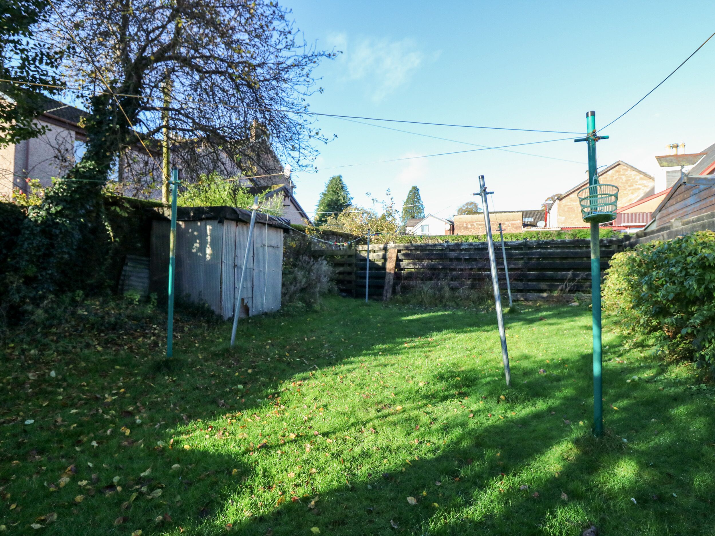 A grassy backyard with a shed, a stone wall, and a metal pole.